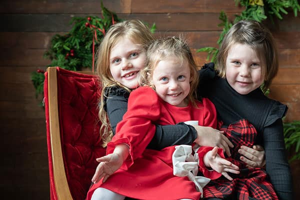 Testimonial-image-blue-horse three girls smiling at camera, in Christmas outfits